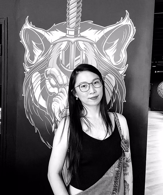Black-and-white portrait of Felicia wearing glasses and a black sleeveless top in front of an illustrated wall.